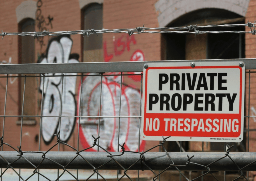 A private property sign on a vacant property, in front of a metal fence and a graffitied building