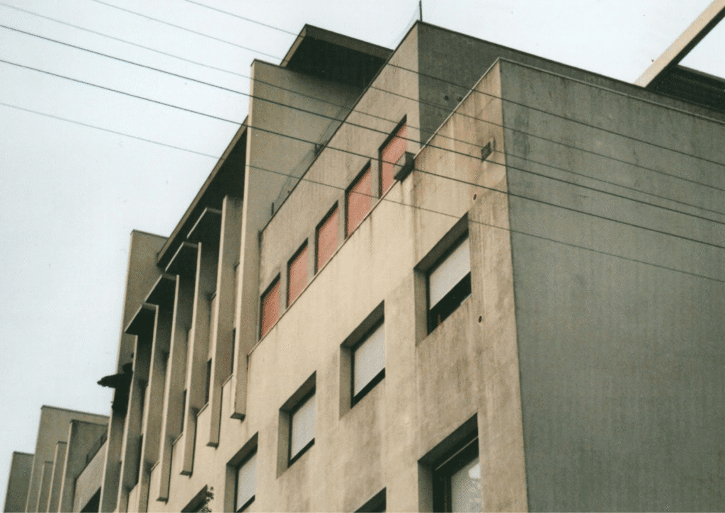 A dirty looking yellowed concrete building with boarded up windows.