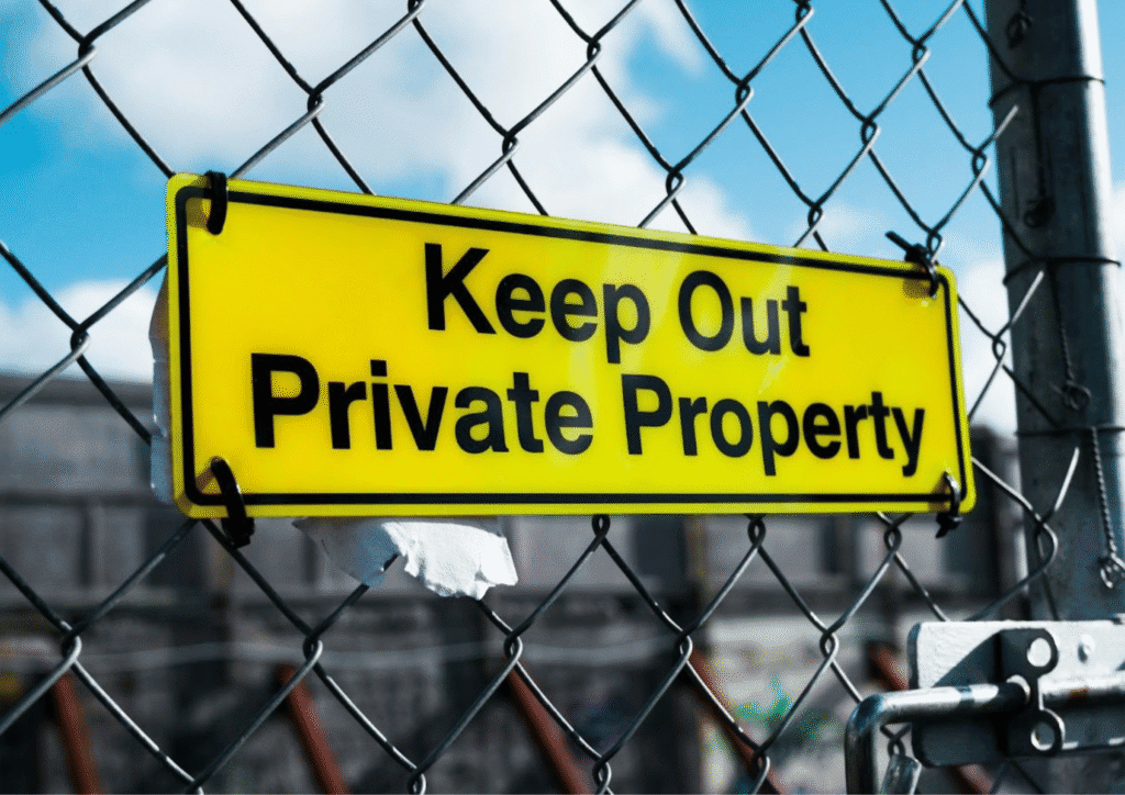A neon yellow sign hung on a wire fence that reads: Keep out, private property