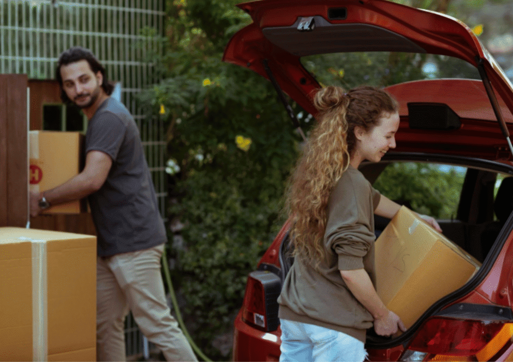 A young, happy couple packing moving boxes into the back of a car.