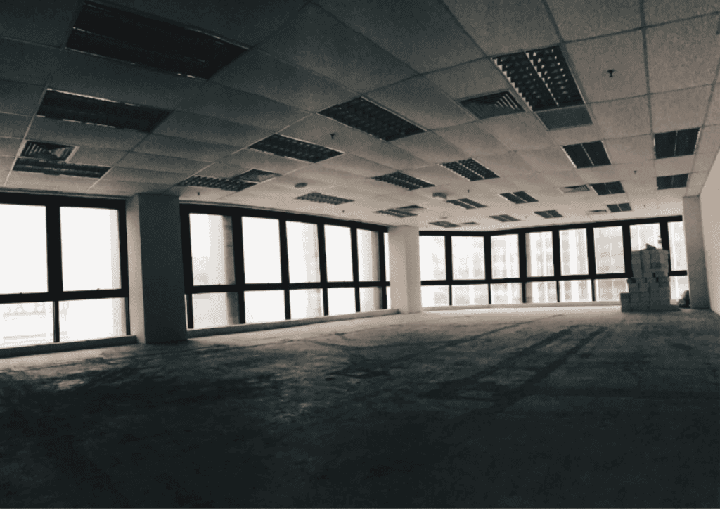 The inside of an empty, abandoned looking building. It's a commercial space with misssing ceiling tiles, large floor to ceiling windows and dark, gloomy lighting.