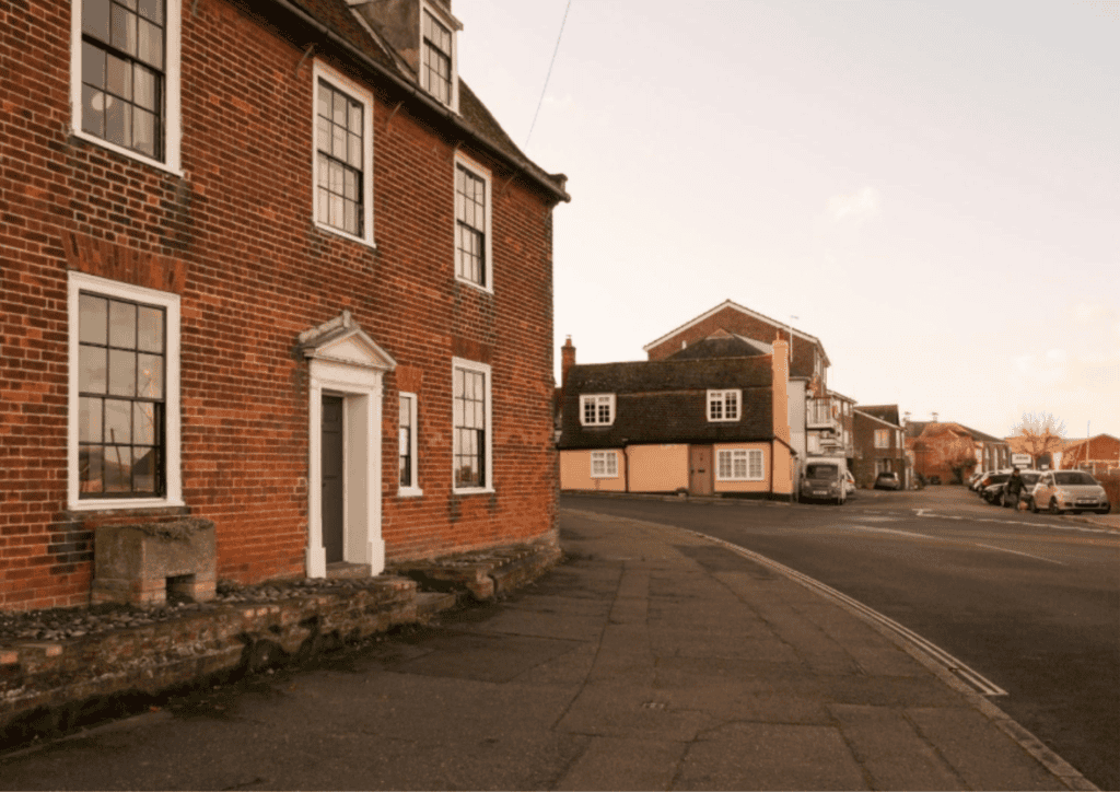 A street corner with a brick building. It has five windows and a door in the centre.